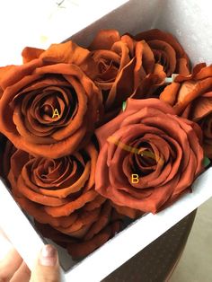 a person holding a white box filled with orange roses and the letters b on it