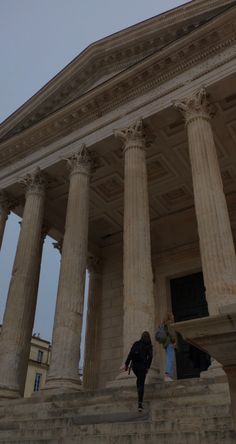 two people are walking up the steps in front of a building with columns and pillars