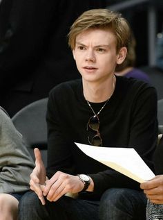 a woman sitting next to a man in a black shirt at a basketball game while holding a piece of paper