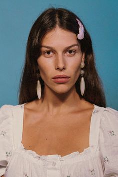 a woman with long hair wearing earrings and a white shirt is looking at the camera