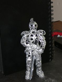 a metal figure sitting on top of a table next to a spiraly notebook holder