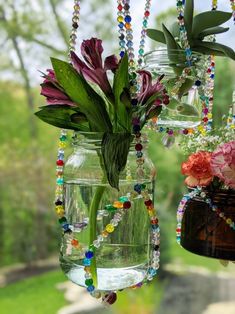 two vases filled with flowers and beads hanging from a window sill in front of a grassy area