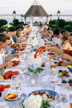 a group of people sitting at a long table eating lobsters