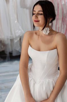 a woman in a white wedding dress looking down at her hand on her hip, with other dresses behind her