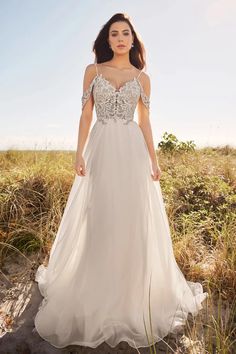 a woman standing in the sand wearing a wedding dress with an open shoulder and beaded bo