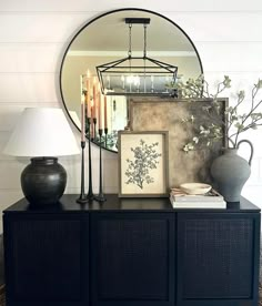 a table with a mirror, vase and lamp on it next to a black dresser