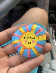 a hand holding a painted rock with a smiling sun design on it's face