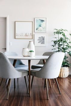 a dining room table with chairs and pictures on the wall above it, in front of a potted plant