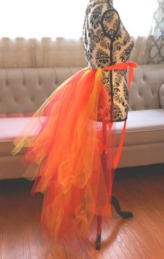 a mannequin with an orange tulle skirt on it's head stands in front of a couch