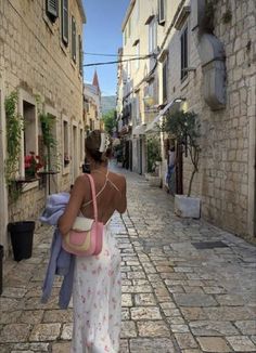 a woman walking down an alley way carrying a pink purse