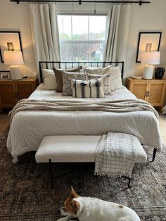 a dog laying on the floor in front of a bed with white sheets and pillows