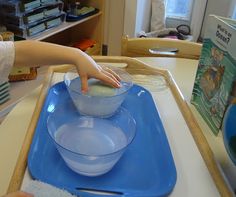 a child is mixing something in a bowl on a blue tray with a book nearby