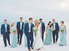 a group of people standing next to each other on top of a sandy beach with the ocean in the background