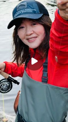 a woman holding a fish while standing next to a body of water with a fishing pole in her hand