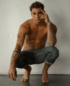 a shirtless man sitting on the floor holding his hand to his face and looking at the camera