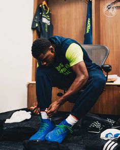 a man tying his shoes while sitting on the floor in front of some sports gear