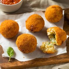 four fried food items on a wooden tray with dipping sauce in a bowl behind them