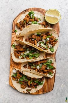 three tacos with meat, onions and cilantro on a wooden platter