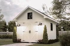 a small white shed with two doors on the front and one door open to let in light