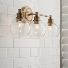 three light bathroom fixture with clear glass globes on the wall and white tile back splash