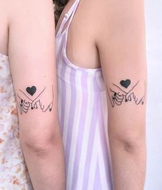 two women with matching tattoos on their arms, one holding the other's arm