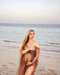 a woman standing on top of a sandy beach next to the ocean wearing a dress