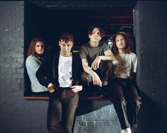 four people sitting on a window sill in front of a brick wall