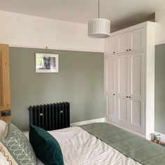 a bedroom with green walls and white bedding, an armoire and radiator