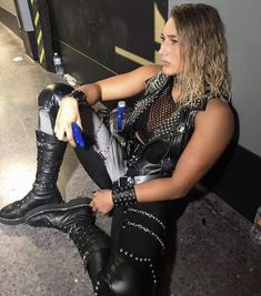 a woman sitting on the ground with her legs crossed and wearing black leather boots, holding a cell phone