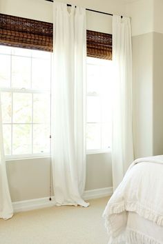 a white bed sitting next to a window in a bedroom under a pair of curtains