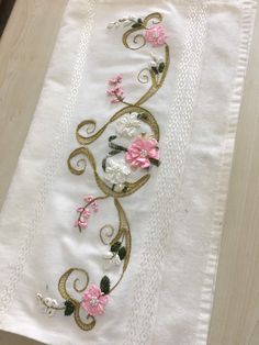 a white towel with pink and white flowers embroidered on it sitting on a wooden table