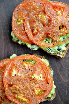 two open faced sandwiches with tomatoes and avocado on toasted bread, sitting on a wooden surface