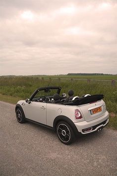 a small white car parked on the side of the road in front of a grassy field