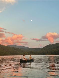 two people in a small boat on a lake with mountains in the background at sunset