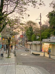 people are walking down the street in front of shops and trees with blossoms on them