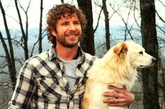 a man holding a large white dog in the woods