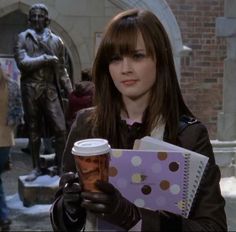 a woman holding a coffee cup in front of a statue