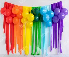 balloons and streamers are hanging on the wall in front of a white backdrop with rainbow colors