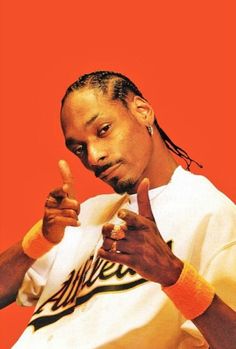 a man with dreadlocks pointing to the side while wearing a white shirt and orange wristband