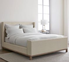 a bed with white linens and pillows in a room next to a large window