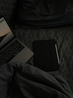 an open laptop computer sitting on top of a bed next to a black book and pillow