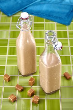 two glass bottles filled with brown liquid sitting on top of a green tile floor