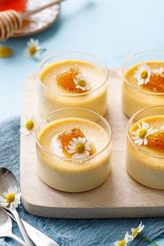 four desserts are arranged in small bowls on a wooden tray with spoons and flowers