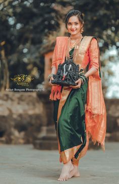 a woman in an orange and green sari holding a black purse with her feet crossed