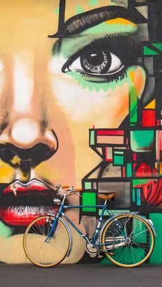 a bicycle parked in front of a colorful wall with a woman's face painted on it