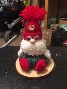 a red and white knitted santa clause sitting on top of a piece of wood