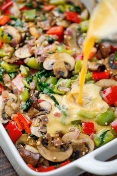 a casserole dish with mushrooms, peppers, and cheese being drizzled over it