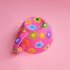 a pink teapot with colorful flowers on it sitting on a pink surface, in front of a white background