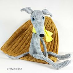 a crocheted gray rat sitting on top of a yellow blanket with blue eyes