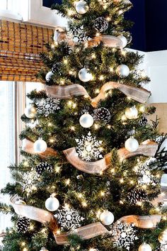 a christmas tree decorated with white and gold ornaments, lights and ribbon on the top